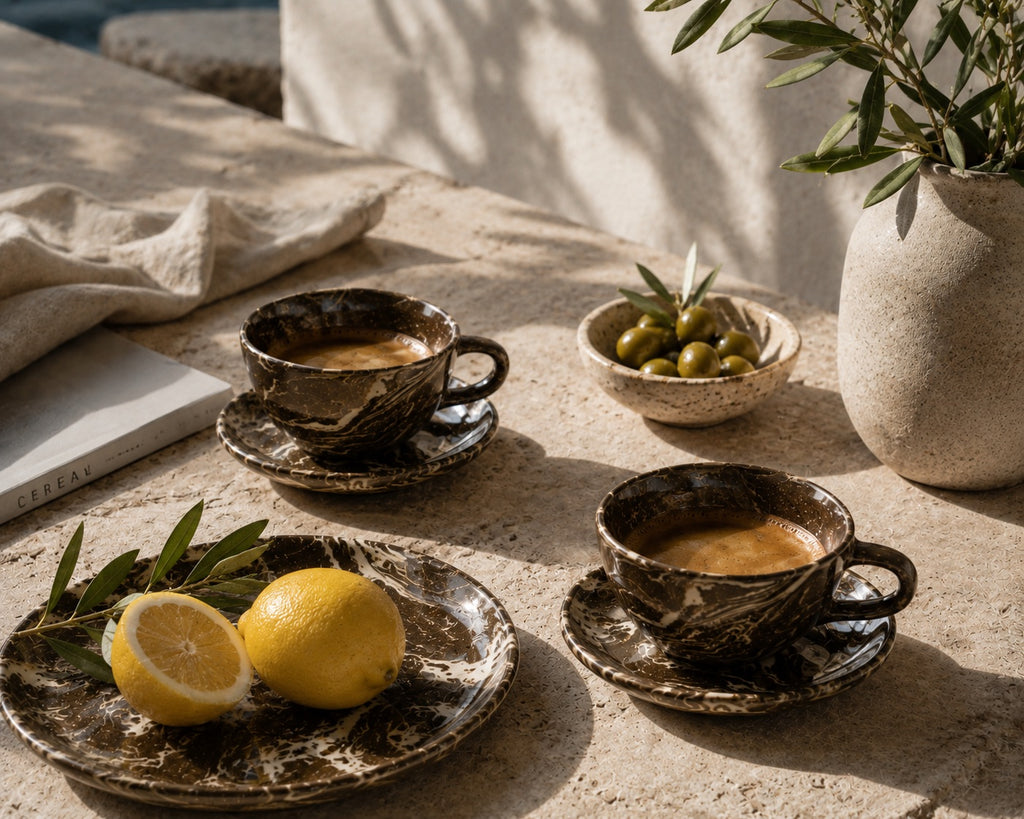 Two cups of coffee on a stone surface with lemons and olives.