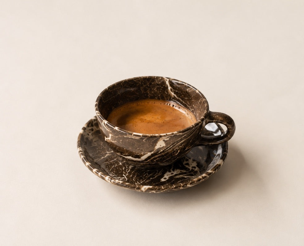 Marble-textured ceramic cup and saucer with a drink on a light beige background
