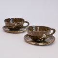 Two marbled brown ceramic teacups with saucers on a light gray background